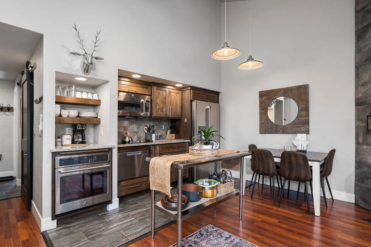 A contemporary kitchen area with a spacious island in the foreground, seamlessly transitioning into an adjacent dining area with a comfortable table and chairs. Modern appliances and a decorative mirror enhance the sense of space, while warm lighting fosters a cozy, social atmosphere.