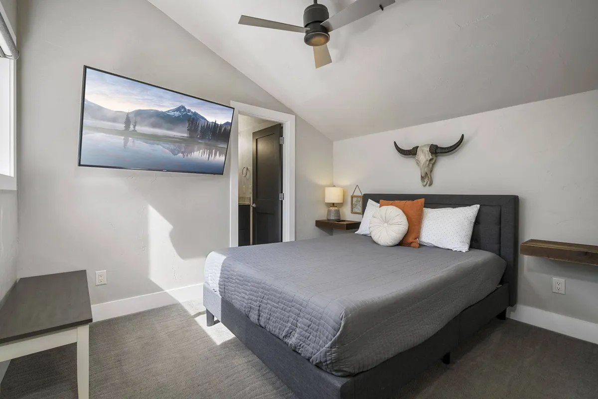 A tranquil bedroom with a plush queen bed, a wall-mounted TV, bedside lamp, and distinctive bull skull decor on the wall. The room exudes comfort and is styled for relaxation, perfectly suited for restful nights after a day of adventure.
