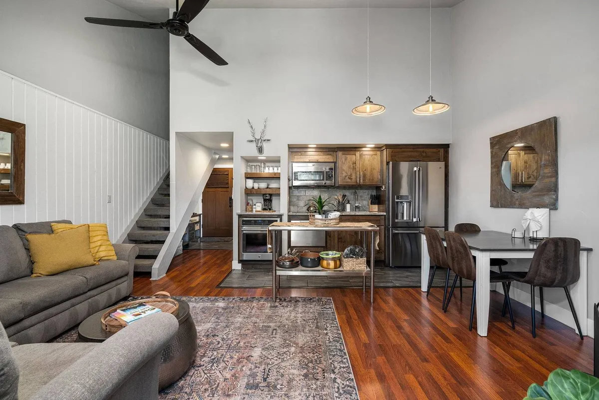 An open-concept main living space with a sofa, kitchen island, dining area, and staircase in view. The space is modern yet cozy, perfect for entertaining, relaxing, and spending quality time with family and friends.