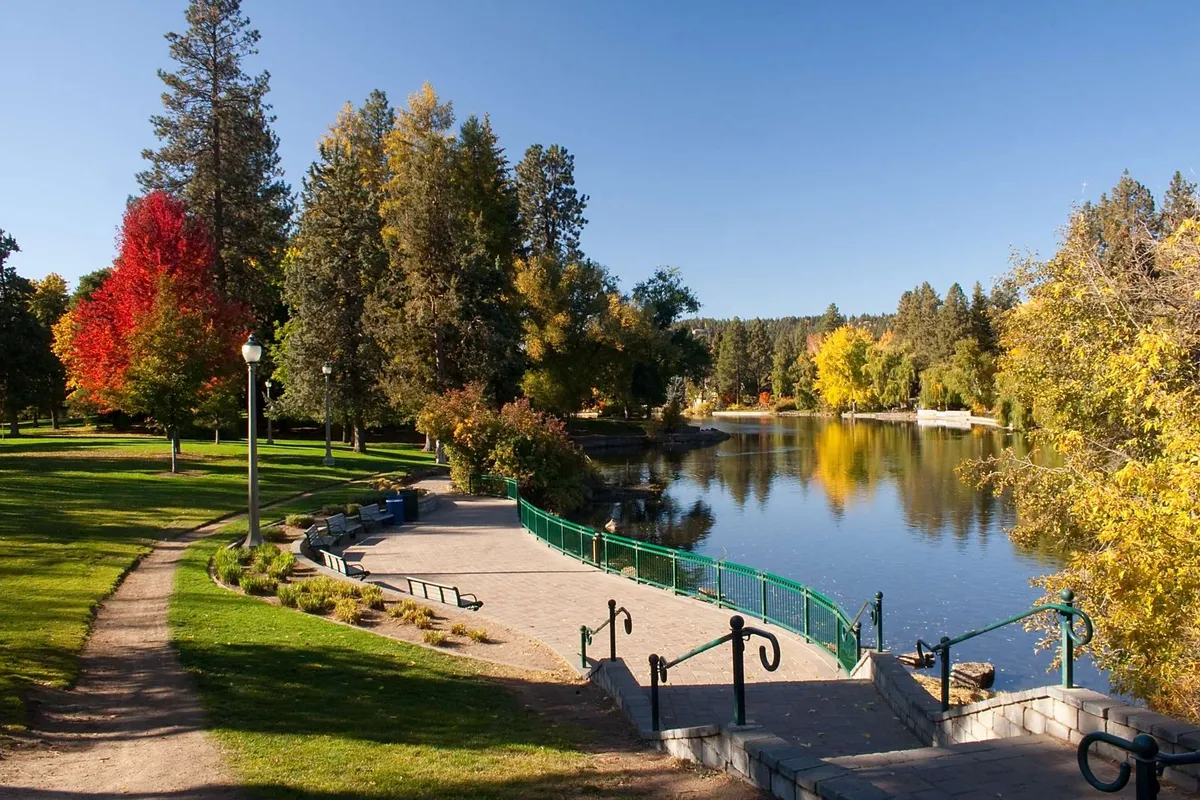 A picturesque exterior scene featuring shimmering water bordered by vibrant autumn foliage. A winding path traces the edge of the water, inviting leisurely walks and moments of relaxation. This tranquil park-like setting hints at the natural beauty and outdoor leisure available near the property.