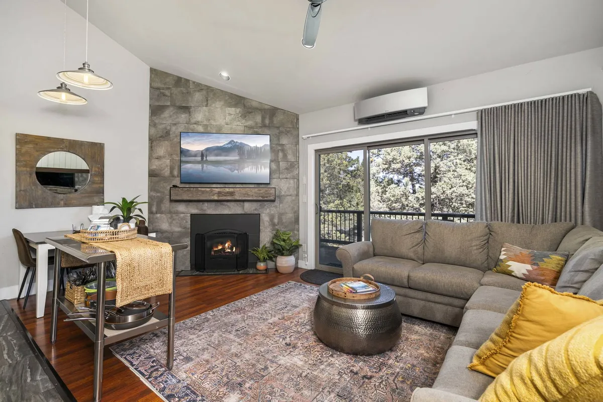 A cozy, open living room featuring a plush sofa, a modern gas fireplace as the focal point, large windows letting in abundant natural light, a textured rug, and tasteful wall art. The inviting seating area is ideal for relaxing, reading, or socializing.