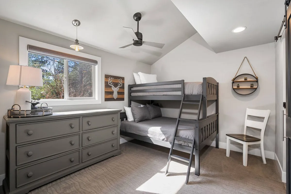 A cheerful second bedroom featuring a twin-over-full bunk bed, a dresser, window, wall art, and a chair for reading or play. The space is playful and welcoming, ideal for families or groups of friends seeking both comfort and fun.